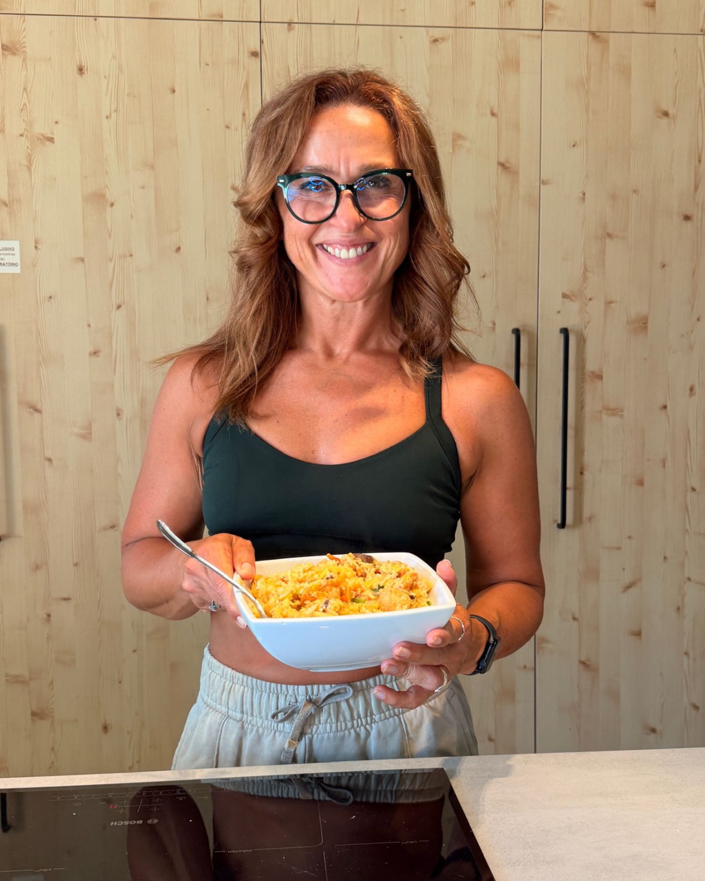 A coach sorri na cozinha com uma taça de comida saudável.